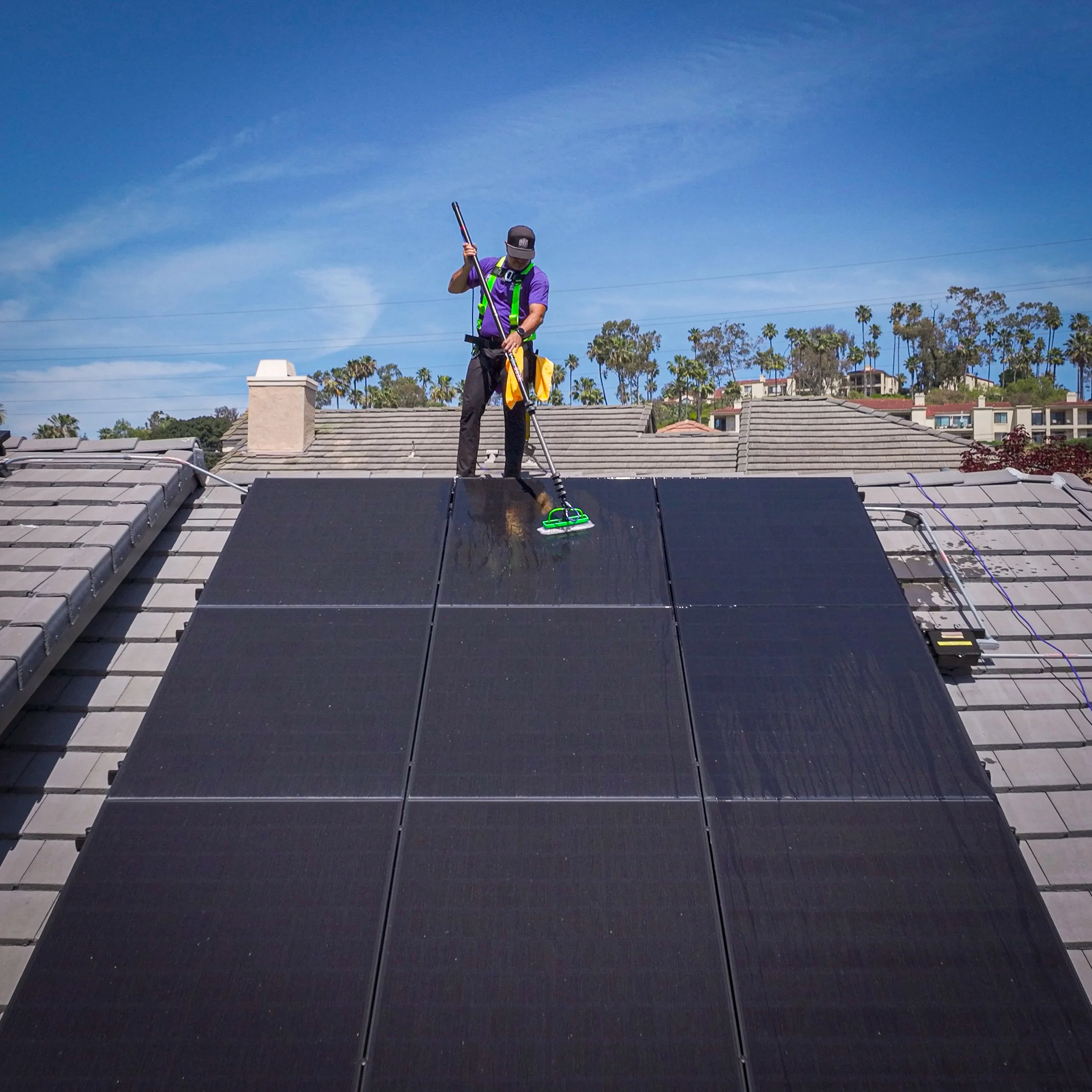 Technician cleaning solar panels on San Diego rooftop with professional equipment