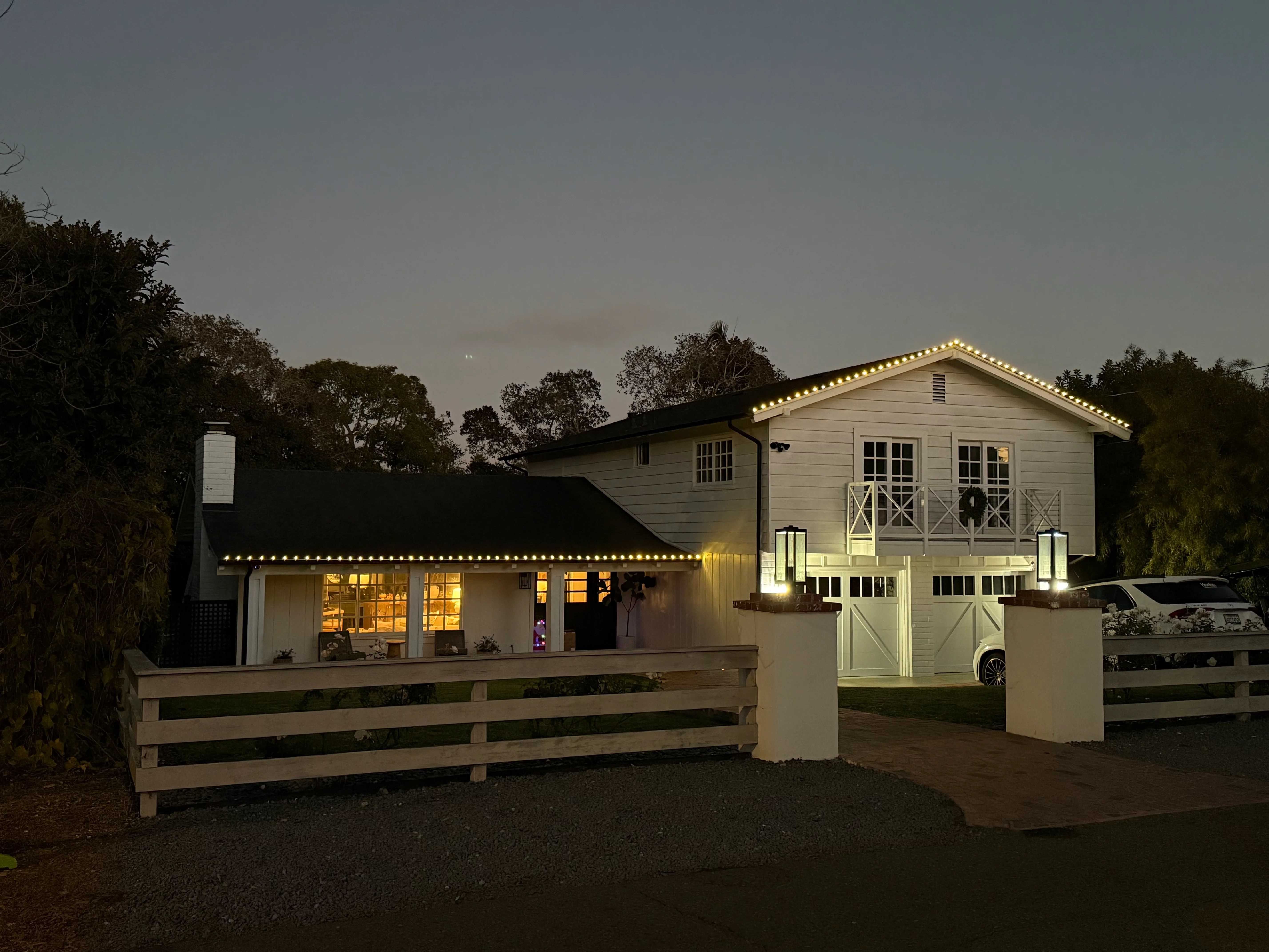 Modern farmhouse at dusk with cleaned windows, white siding, and decorative landscape lighting