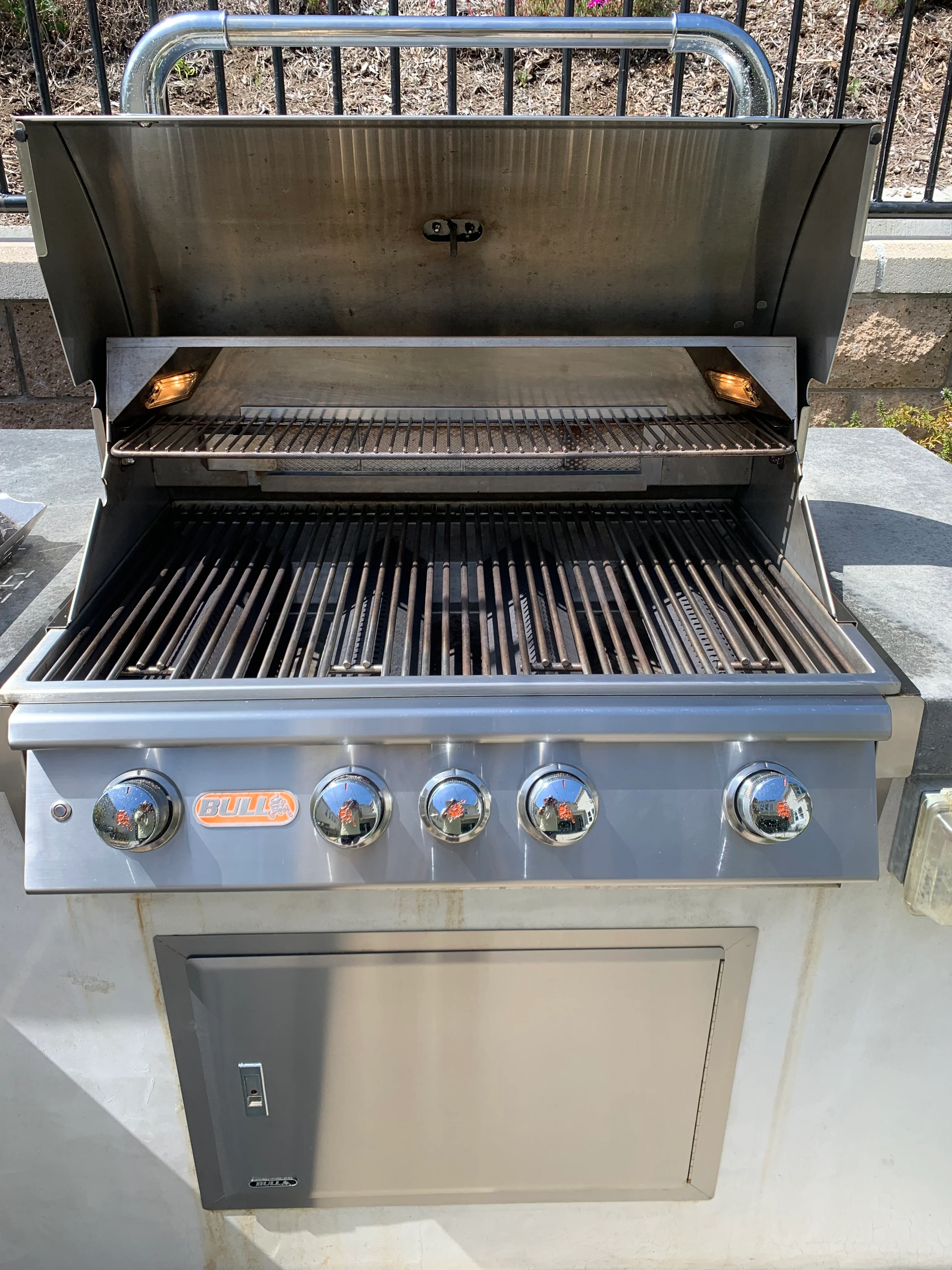 Stainless steel five-burner built-in grill with polished knobs and open lid showing clean grates