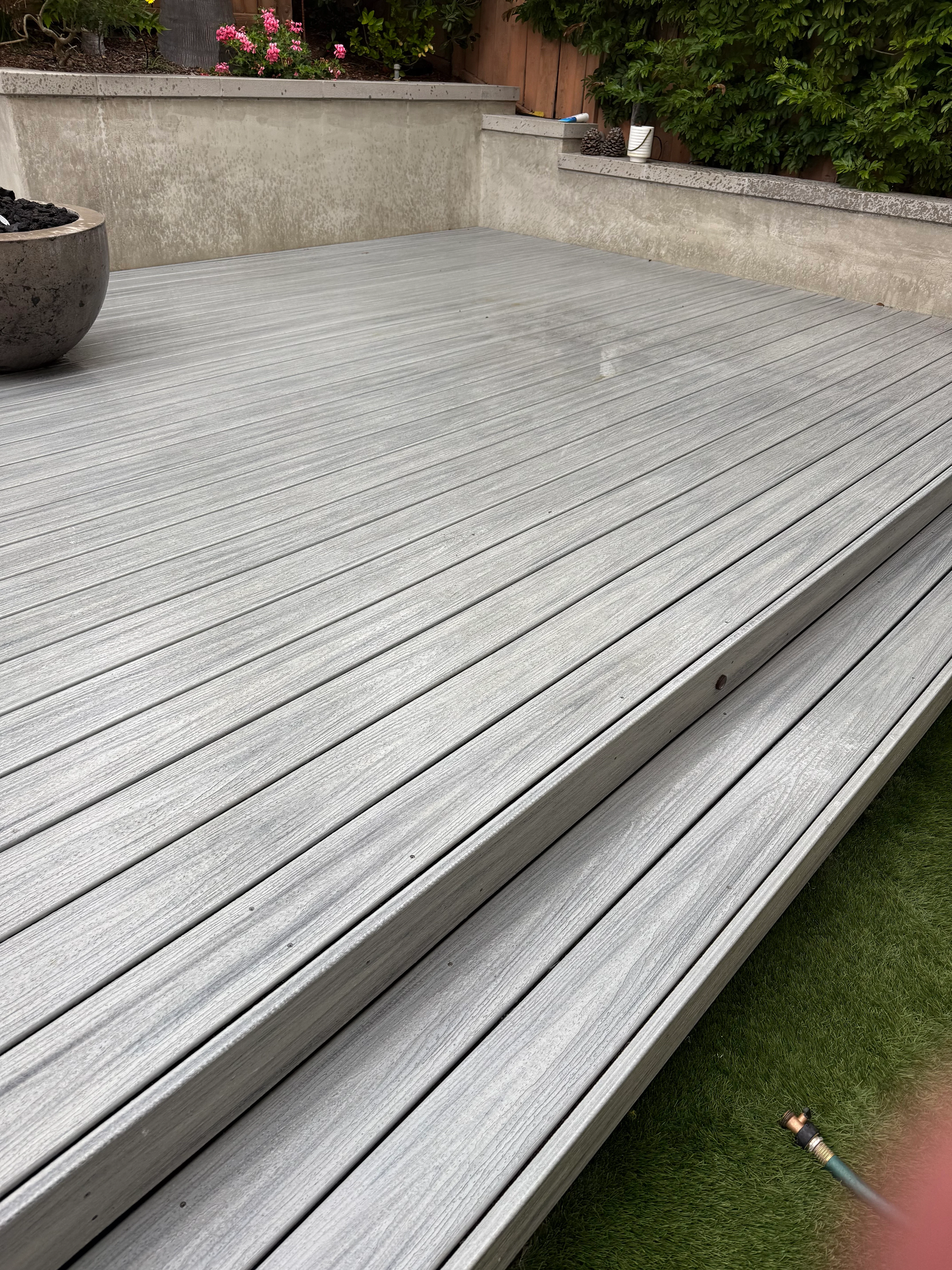 Clean gray composite deck with linear board pattern, concrete walls, and pink flowering plants