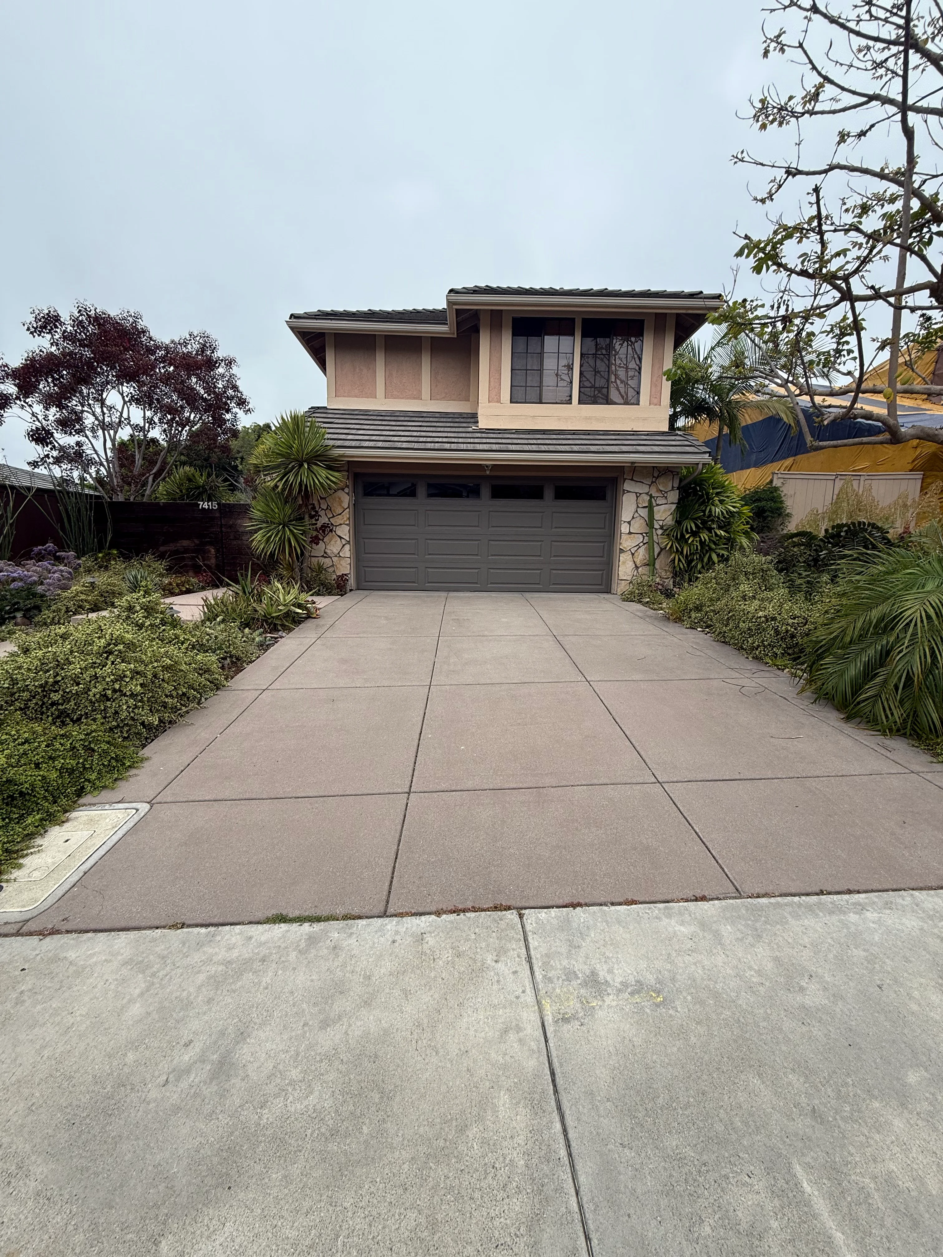 Clean concrete driveway with large pavers in front of modern two-story home with landscaping