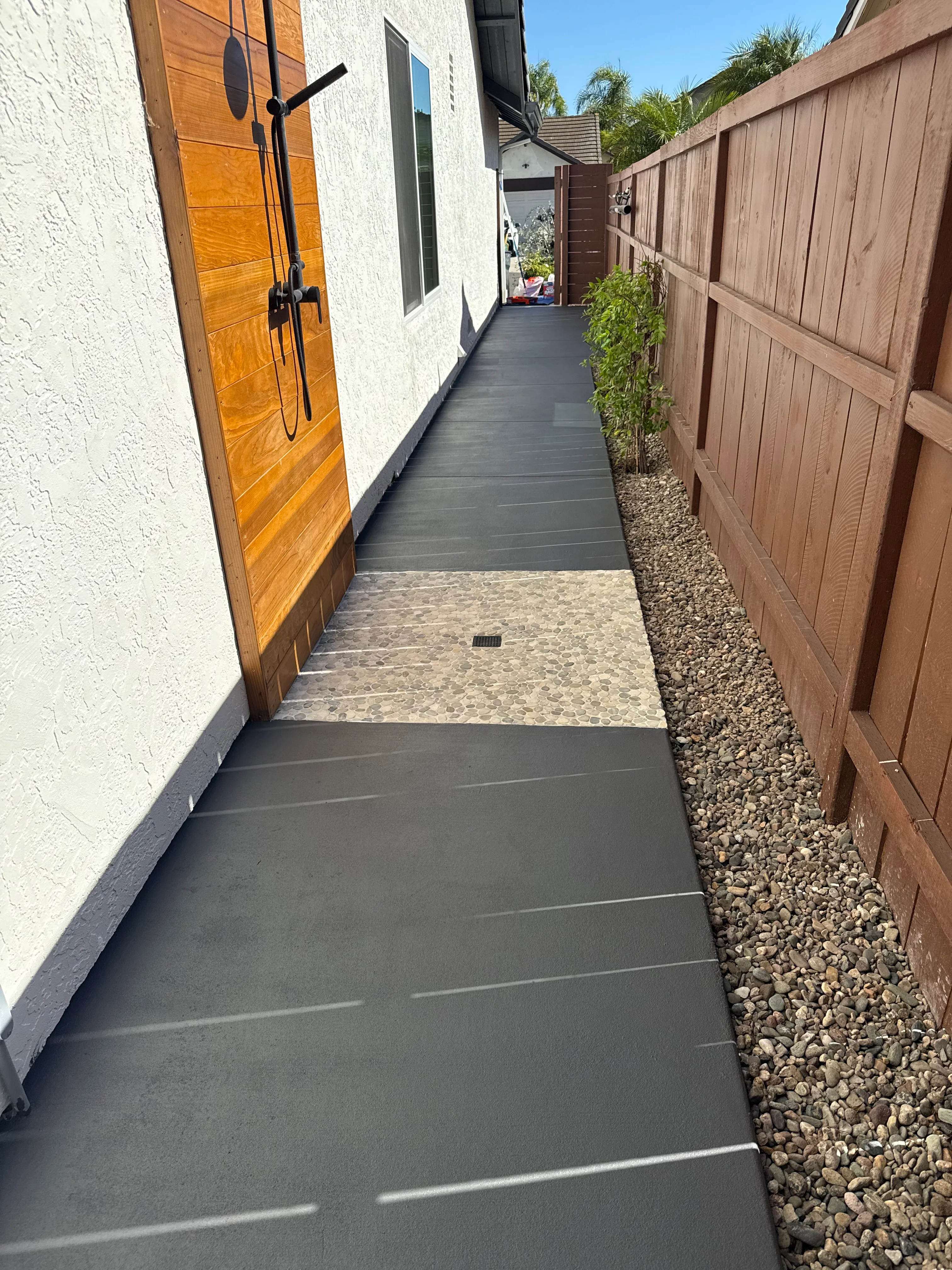 Clean dark composite deck pathway with stone pavers and gravel border alongside modern home