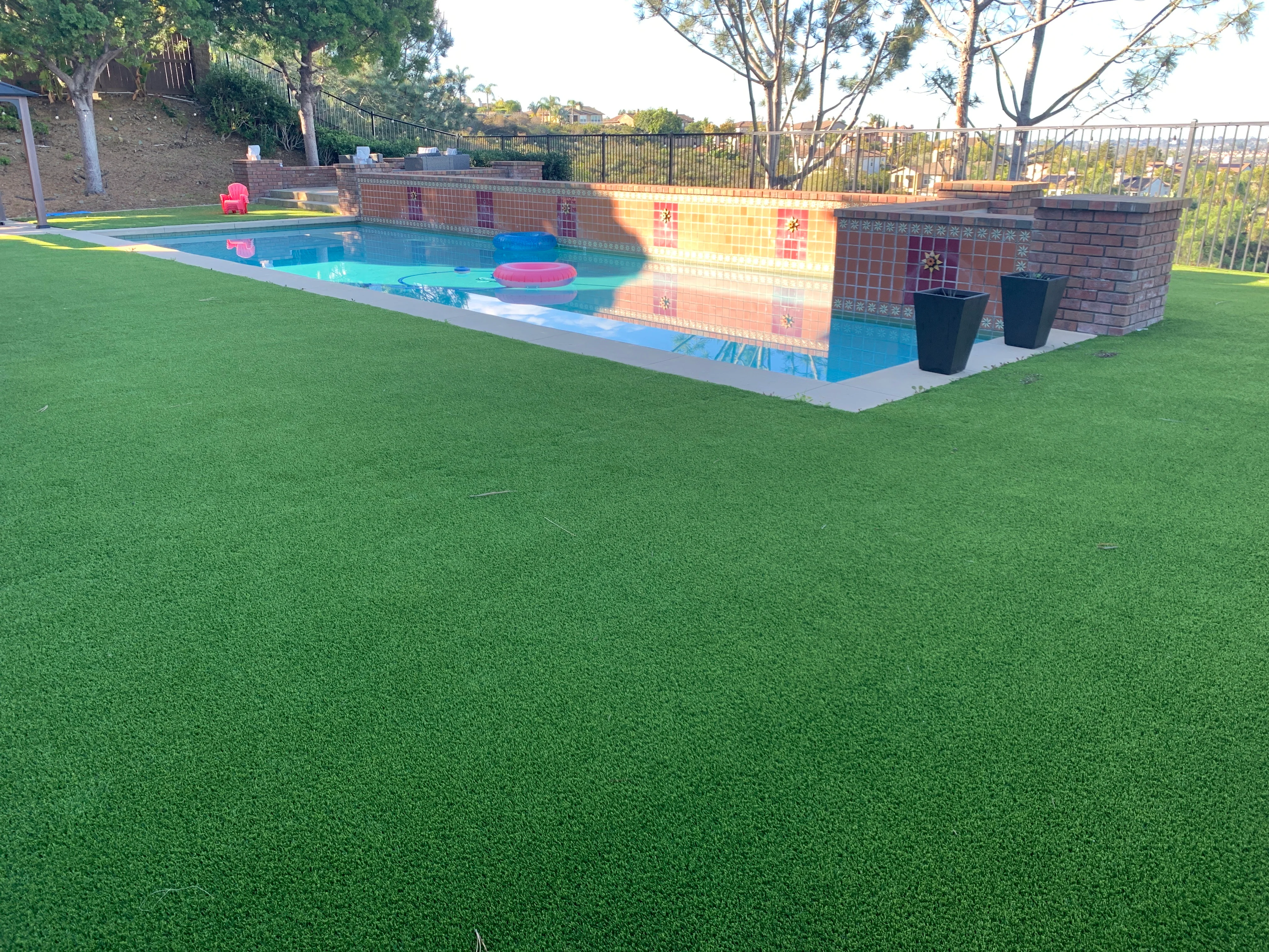 Cleaned artificial turf surrounding a blue pool with brick walls and metal fencing in San Diego