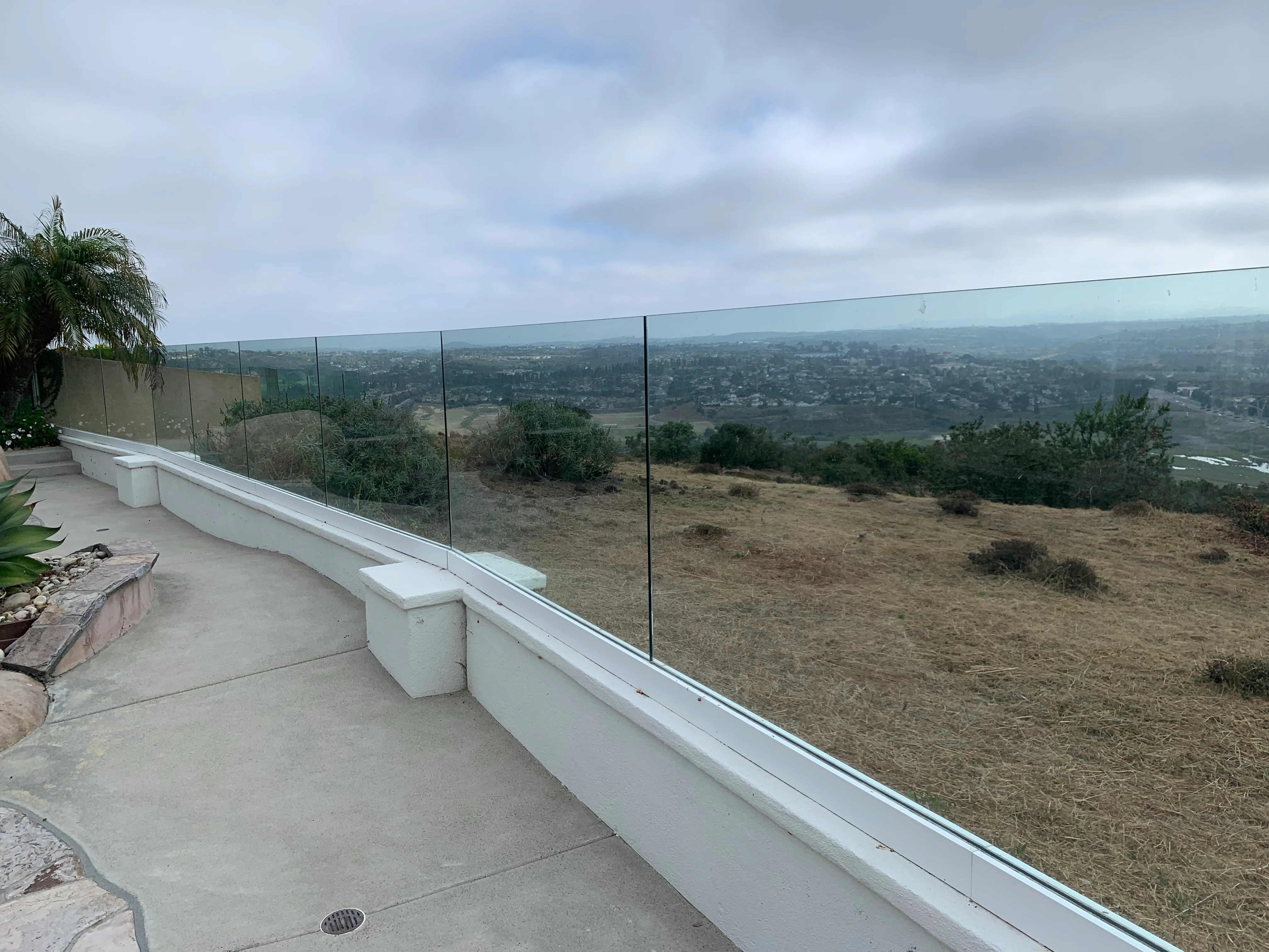 Clean frameless glass railing on deck with valley view, white concrete base and seating area