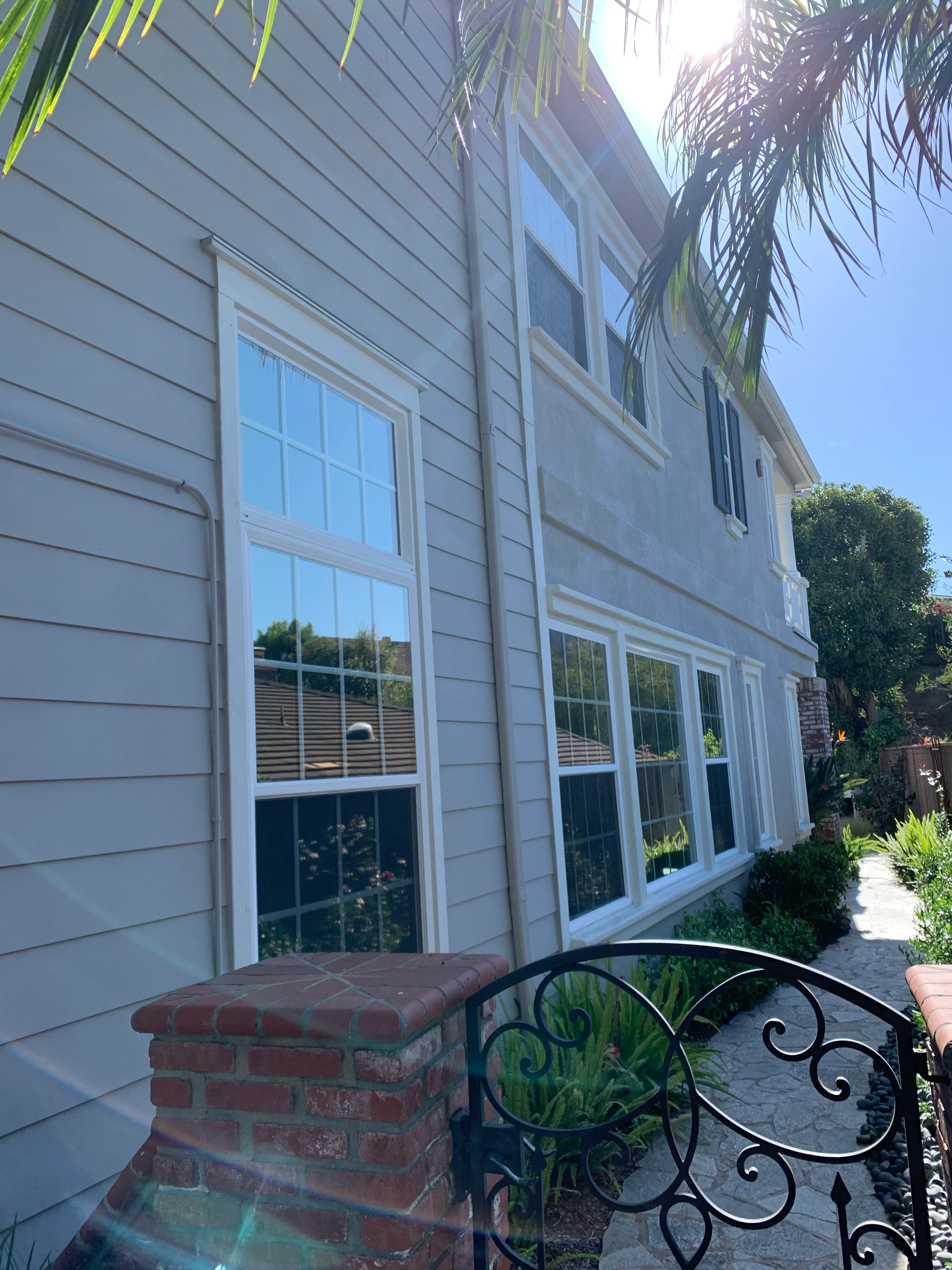Clean windows on white-sided residential home with palm trees and brick chimney
