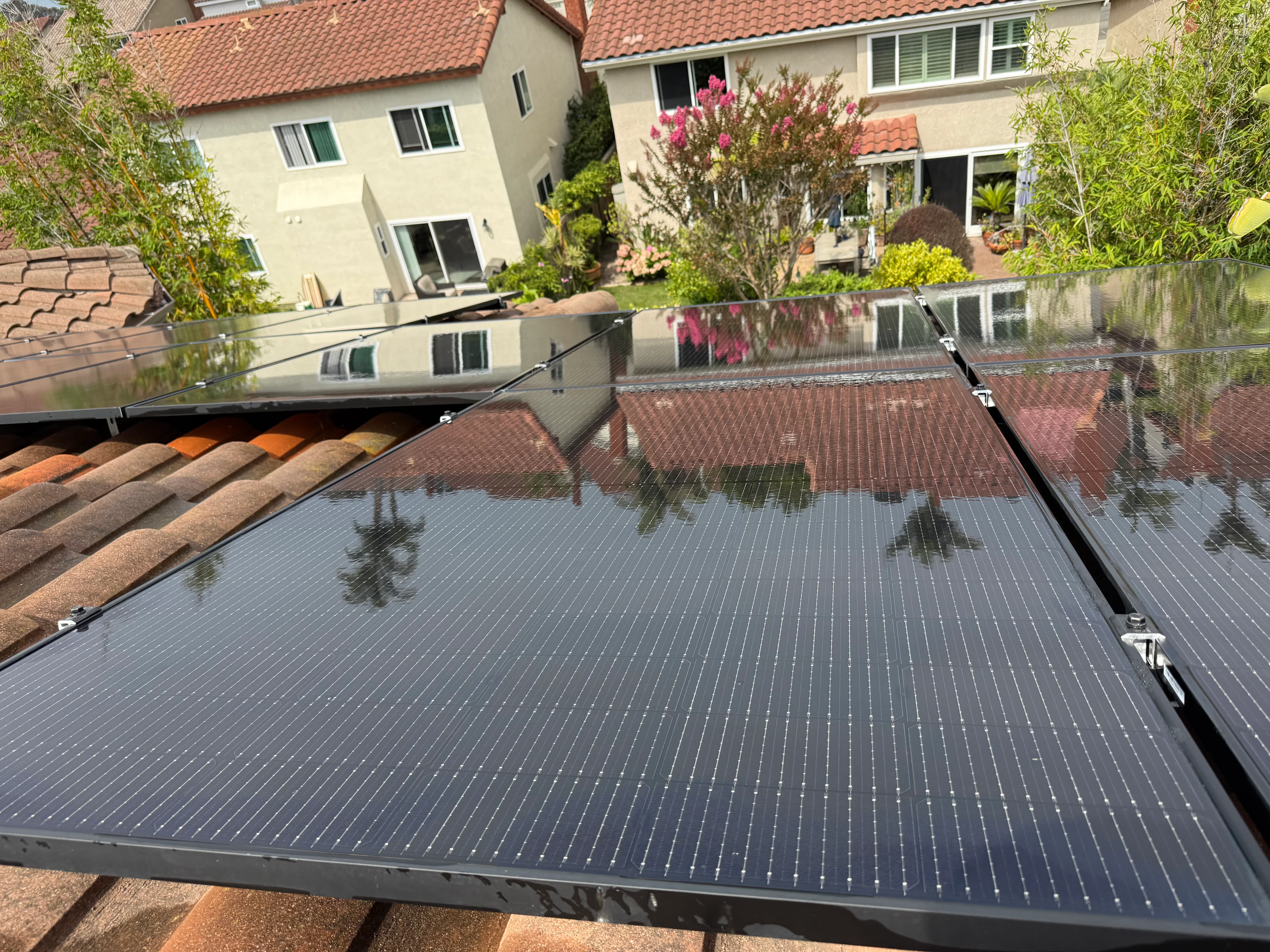 Clean solar panels on residential roof with clay tiles and landscaped backyard