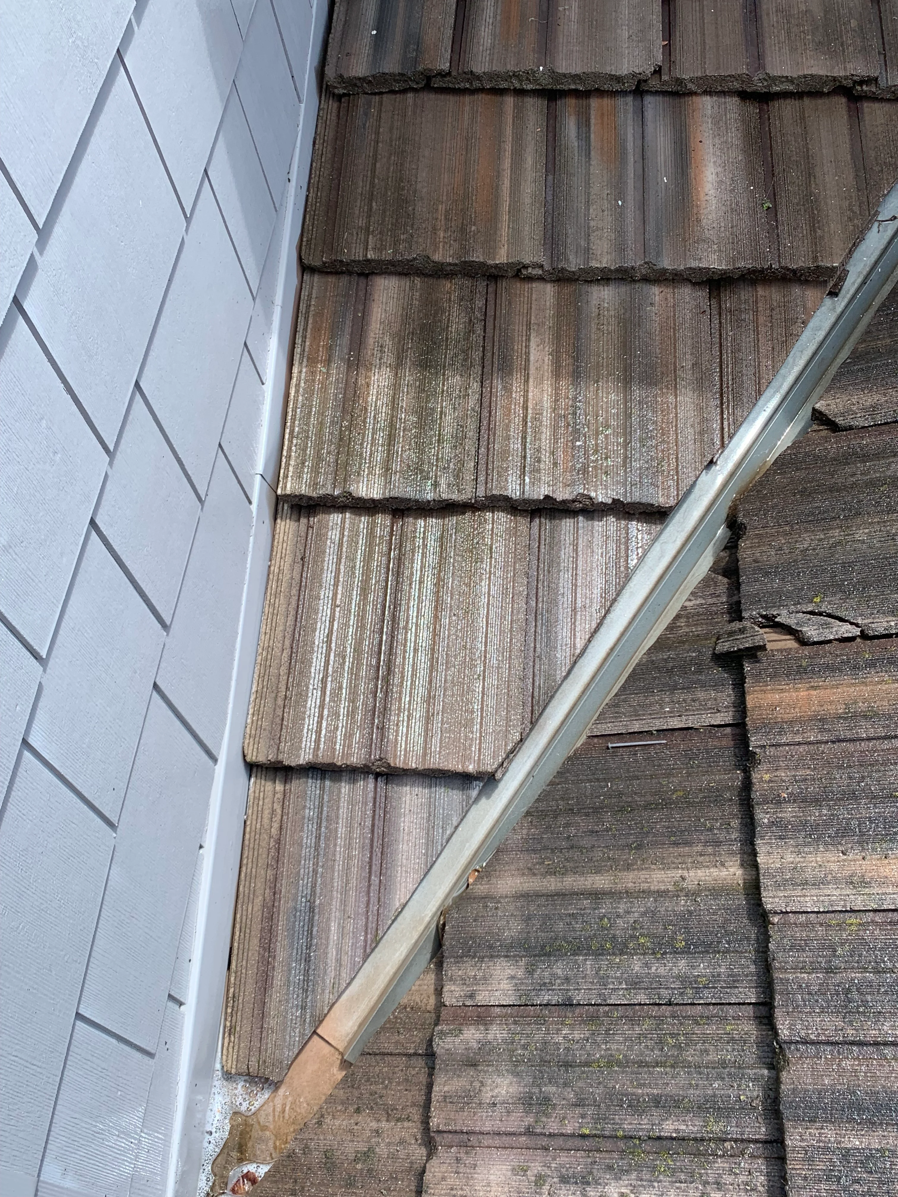Cleaned wood shake roof tiles next to white siding with metal gutter